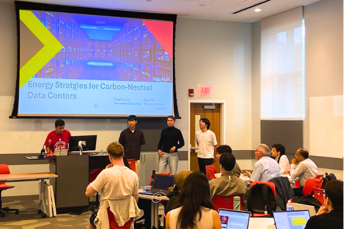 A group of four students presents their final project to the larger group. A slide behind them that says, 'Energy Strategies for Carbon-Neutral Data Centers.'