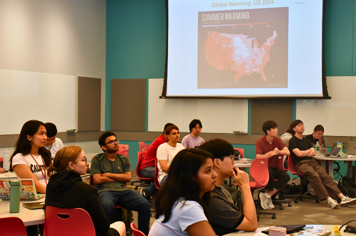 seminar students listen intently to a presentation. A slide says 'Global Warming: US 2024 and shows a map of the U.S., indicating summer warming.