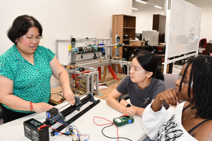 Mildred Pates with UMD engineering students. Her prototype sits on a table.